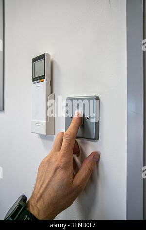 Person switching a wall light on or off in a home or office environment. The scene features a standard wall light switch alongside a white air con Stock Photo