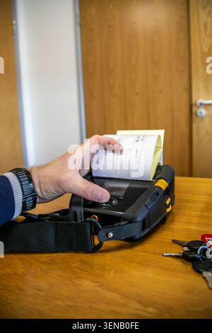 Person checking or picking up a label from a mobile printer used for printing barcode labels and receipts in a warehouse or logistics environment. Stock Photo