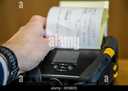 Person checking or picking up a label from a mobile printer used for printing barcode labels and receipts in a warehouse or logistics environment. Stock Photo