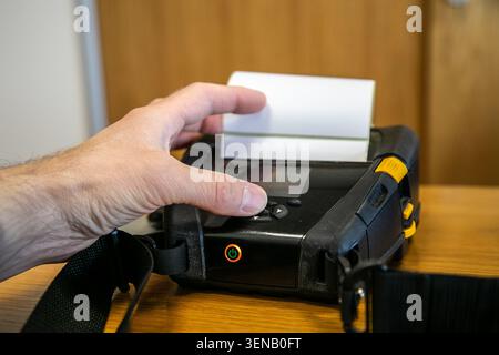 Person checking or picking up a label from a mobile printer used for printing barcode labels and receipts in a warehouse or logistics environment. Stock Photo