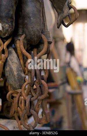 Rusty chains hang heavy from worn leather boots. Worn leather straps suggest rugged use. Background blur hints at outdoor workshop setting. Texture de Stock Photo
