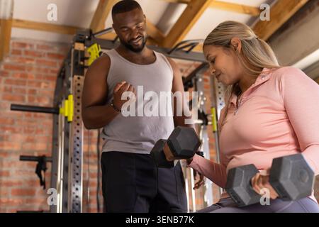 African American trainer and client doing biceps curls on home gym bench with black hex dumbbells Stock Photo