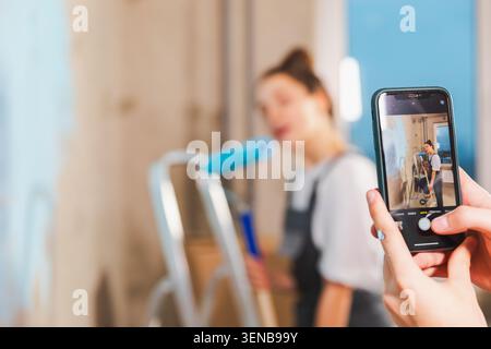 Couple in new home. Man taking photo woman during repair works painting walls. Happy family bloggers painting wall make selfie in social network. Happy family doing home renovation. DIY renew home Stock Photo