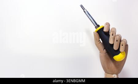 Wooden artist mannequin hand holding a flathead screwdriver isolated on white background with copy space. Image representing maintenance, repair. Stock Photo