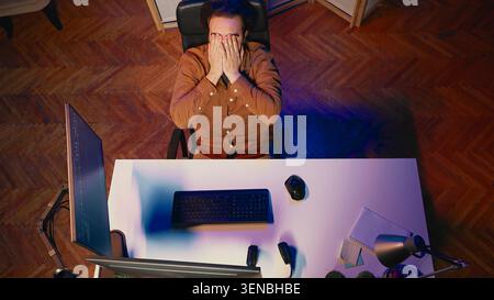 Top-down view of software engineer putting face in hands in frustration while updating binary code script on computer, receiving errors. IT worker exasperated by annoying bugs while programming. Stock Photo