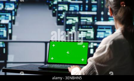 Adept computer scientist in server farm housing high end systems capable of quickly and efficiently performing complex computations and data analysis, using mockup laptop to avoid hazards. Stock Photo