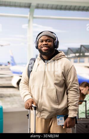 African american traveler, air travel concept, carrying luggage by departure gate, in airport terminal. Black man excited about his vacation by plane, checking flight details before boarding. Stock Photo