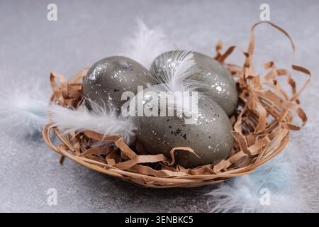 Easter eggs in wicker nest with feathers rustic background Stock Photo