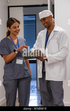 Medical coworkers reviewing tablet chart in hospital hall, wearing gray scrubs and ID badges Stock Photo