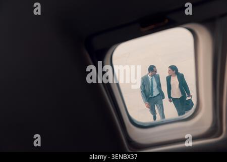 Two confident business executives walking and talking on airport tarmac viewed through a private jet window with natural copy space ideal for Stock Photo