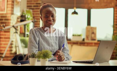 Woman writing down important ideas for online freelancing career, taking notes on notebook and creating teleworking planner, African american freelancer productivity, Handheld shot. Stock Photo