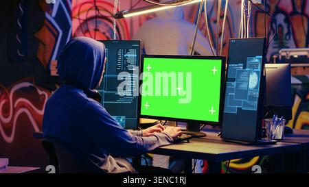 Hackers using green screen PC to code malware designed to exploit network backdoors, Cybercriminals use mockup monitor while bypassing security measures in graffiti painted bunker. Stock Photo