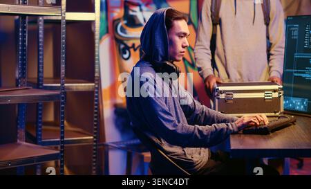 Hacker in abandoned warehouse providing SSD device filled with valuable data after using phishing technique that tricks users into revealing sensitive information. Stock Photo