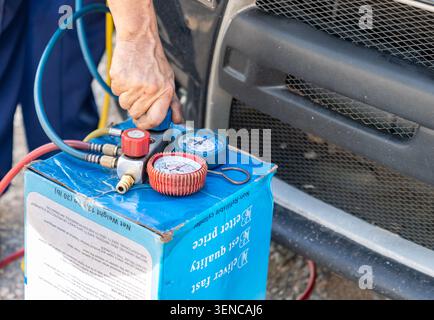 Automotive technician using a professional AC manifold gauge set and refrigerant cylinder to diagnose and recharge a vehicle cooling system. Stock Photo
