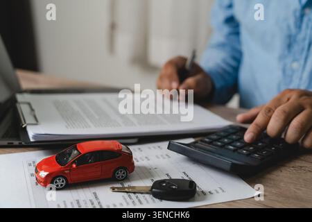 Person calculating vehicle expenses with a calculator while reviewing documents beside a model car and car key, supporting automotive budgeting, finan Stock Photo