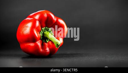 Vibrant red sweet pepper with green stem on dark surface, professional studio shot Stock Photo