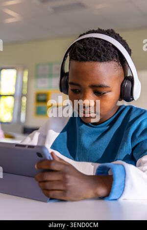 African American schoolboy sitting at desk in class using tablet wearing white headband headphones Stock Photo