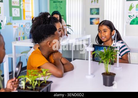 Diverse teacher and elementary students exploring plants, using wind models and tablet at table Stock Photo