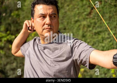 Man focusing and concentrating while shooting a bow and arrow during outdoor training Stock Photo