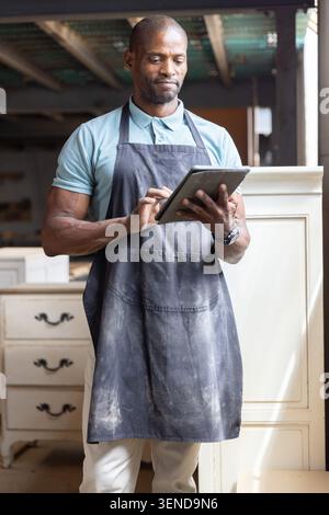 African American man using digital tablet and inspecting wooden cabinets in workshop Stock Photo
