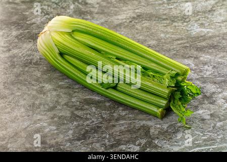 Bunch of fresh green celery stalks with leaves resting on textured gray stone surface, healthy vegetable ingredient for cooking, raw produce, close up Stock Photo