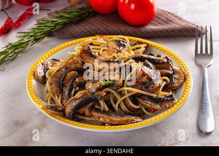 Delicious spaghetti pasta topped with fried mushrooms served on a white plate with yellow rim. Fresh rosemary sprig red tomatoes in background. Rustic Stock Photo