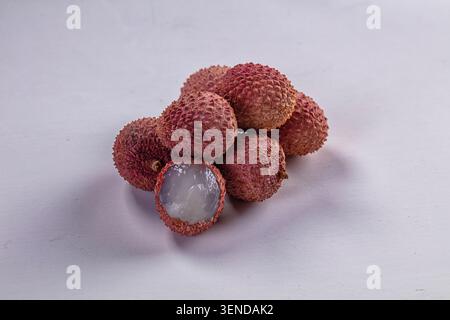 Cluster of ripe lychee fruits with rough pink skin and one peeled revealing juicy white flesh. Studio lighting highlights texture and freshness. Ideal Stock Photo