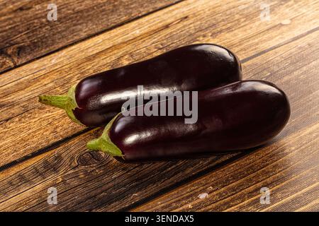 Two glossy purple eggplants with green stems resting on rustic brown wooden surface. Fresh organic vegetables for cooking. Healthy food concept. Natur Stock Photo