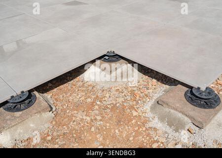 Top down angle shot showing the corner joint of four large grey terrace tiles resting on a single black adjustable plastic pedestal support over a Stock Photo