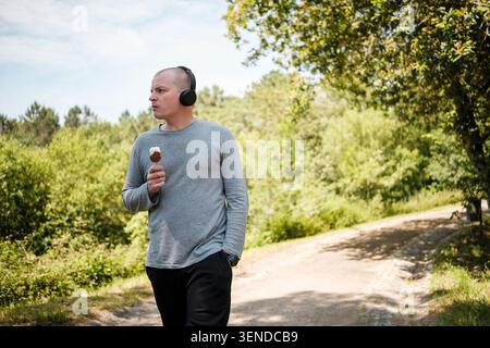Man enjoying a summer walk in the park while eating ice cream on a stick and listening to music Stock Photo