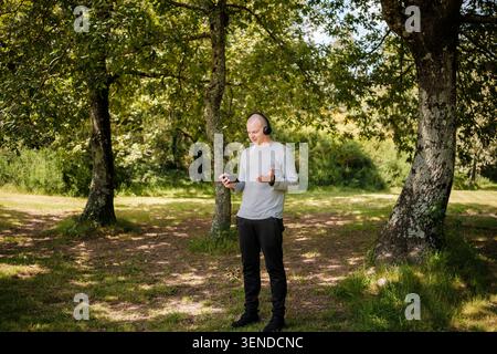 Man standing in a park, holding a smartphone and wearing headphones, engaging in a video call Stock Photo