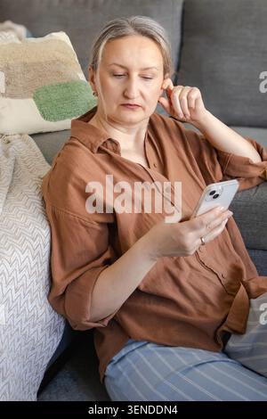 Woman using smartphone at home, interacting with AI assistant for everyday tasks. Natural lifestyle scene showing digital technology, smart solutions, Stock Photo