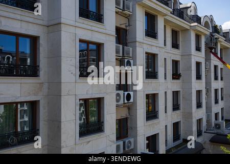 HVAC Technician Inspecting Air Conditioning Units from Aerial Work Platform on Residential Building Facade Stock Photo