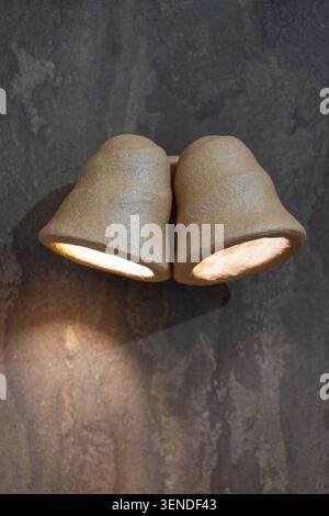 Handcrafted dual ceramic wall sconce with warm LED illumination mounted on textured dark plaster wall in modern minimalist interior Stock Photo