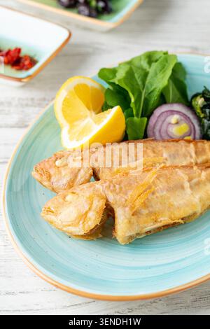 Fried red mullet with lemon, lettuce and vegetables served on rustic blue plate Stock Photo