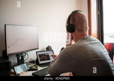 Man analyzing stock market charts on multiple screens in a modern home office Stock Photo