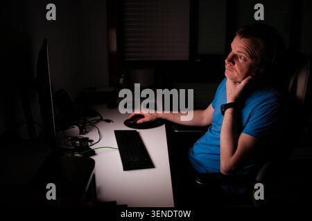 Man feeling weary and concentrating while working late at night on his computer Stock Photo