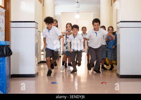 Group of cheerful elementary school students running and playing together in a bright school corridor. Stock Photo