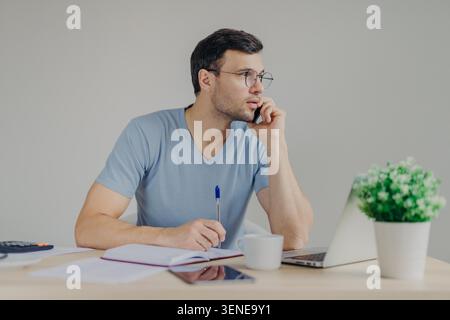 Young man writes notes beside laptop while working at home desk Stock Photo