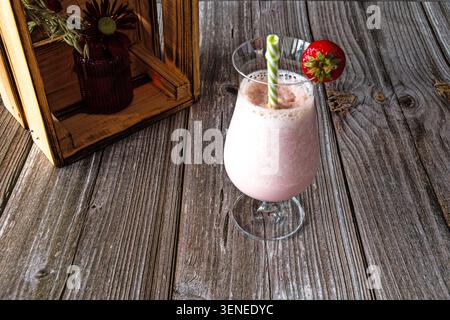 Strawberry milkshake in a glass with drinking straw and fresh strawberry on a rustic wooden table with decorative wooden crate. Stock Photo