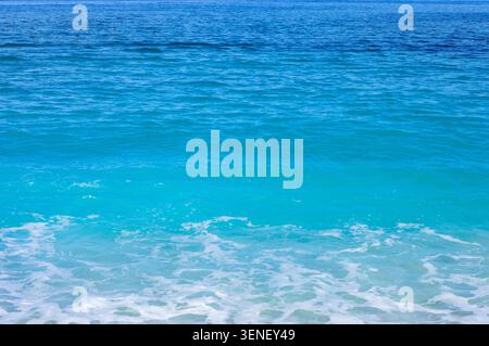 A beautiful gradient of clear, bright turquoise ocean water rippling near the shore, transitioning into a deeper blue Stock Photo