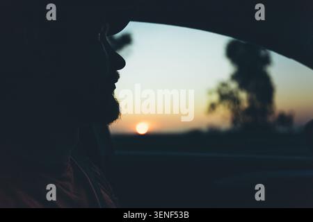 Silhouette of bearded man looking through car window at golden sunset during a peaceful evening road trip. High quality photo Stock Photo