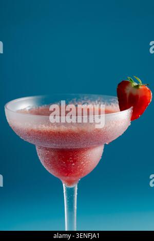 Frozen strawberry daiquiri cocktail in a glass garnished with a fresh berry slice on a blue background Stock Photo