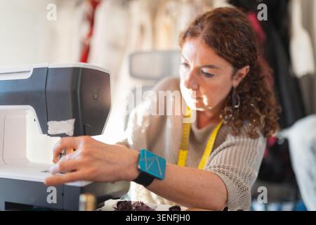 Woman using sewing machine in workshop during daylight hours for fabric and clothing projects Stock Photo