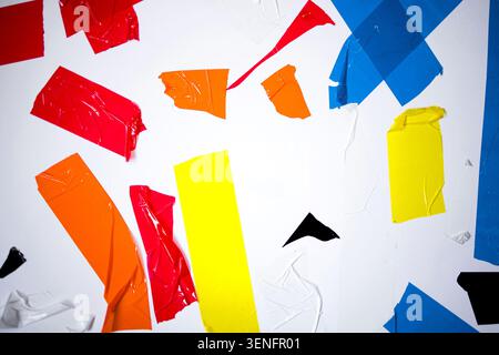 Torn pieces of colorful adhesive tape in various shades are scattered across a clean white background, forming an abstract visual arrangement Stock Photo