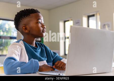 African American child student sitting at school desk using silver laptop wearing blue sweatshirt Stock Photo