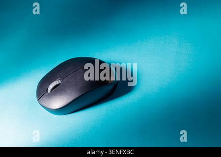 A sleek matte black wireless computer mouse resting on a vibrant cyan background with sharp directional light and shadow, representing modern technology, digital workflow, and office productivity. Stock Photo