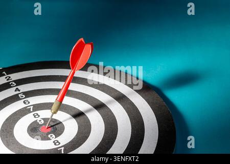 A horizontal perspective showing a single red dart hitting the exact red bullseye of a dartboard with copy space on the blue background, illustrating target marketing, laser focus, and absolute business victory. Stock Photo