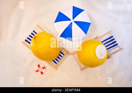 Two lemons placed on small beach chairs under a blue and white umbrella, with a lifebuoy nearby, creating a playful summer scene Stock Photo