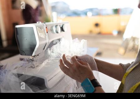 Sewing fabric with a sewing machine in a workspace during daylight hours Stock Photo